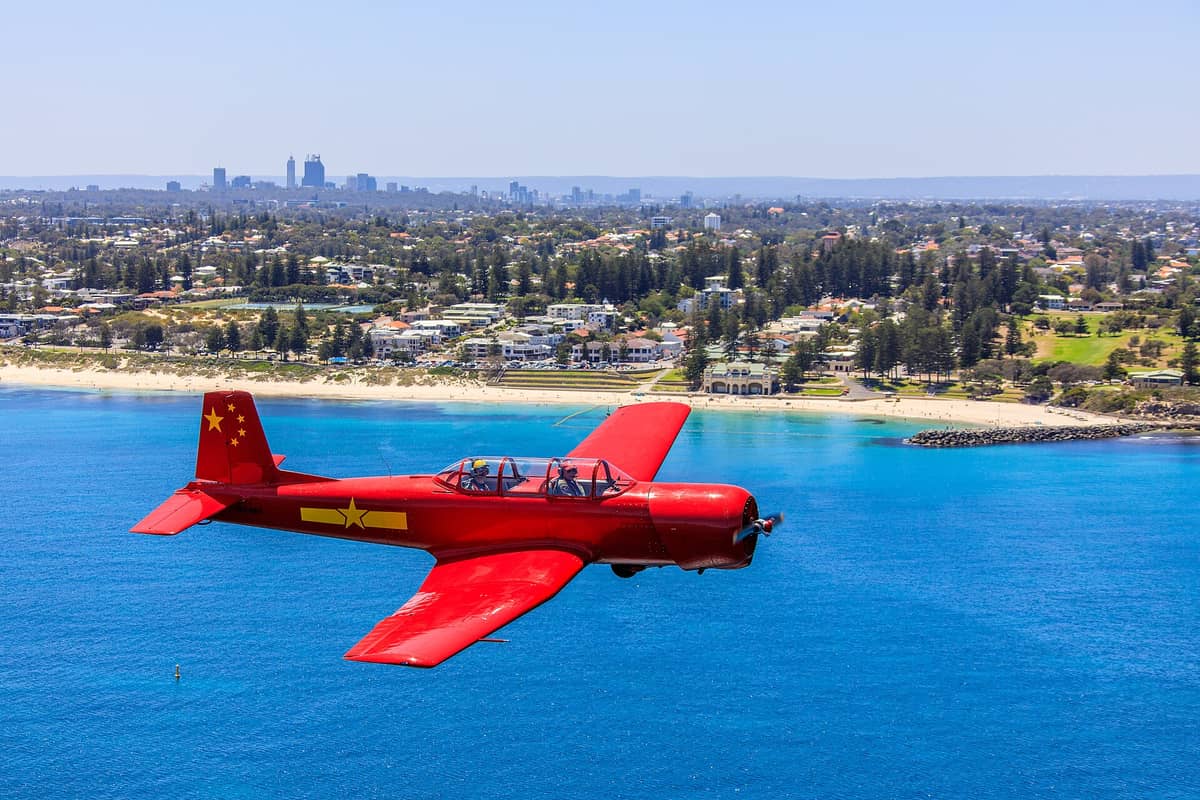 Ein weiter Blick auf den Cottesloe Beach in Perth mit klarem blauem Wasser, Sandstrand, Graspark und der Skyline der Stadt in der Ferne