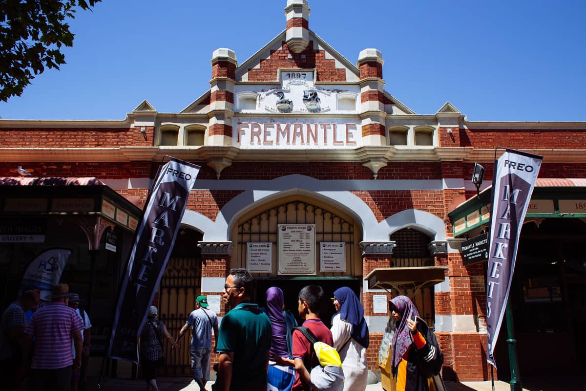 People walking outside the historic Fremantle Markets building with red brick facade and 'Fremantle' sign in Perth, Australia.