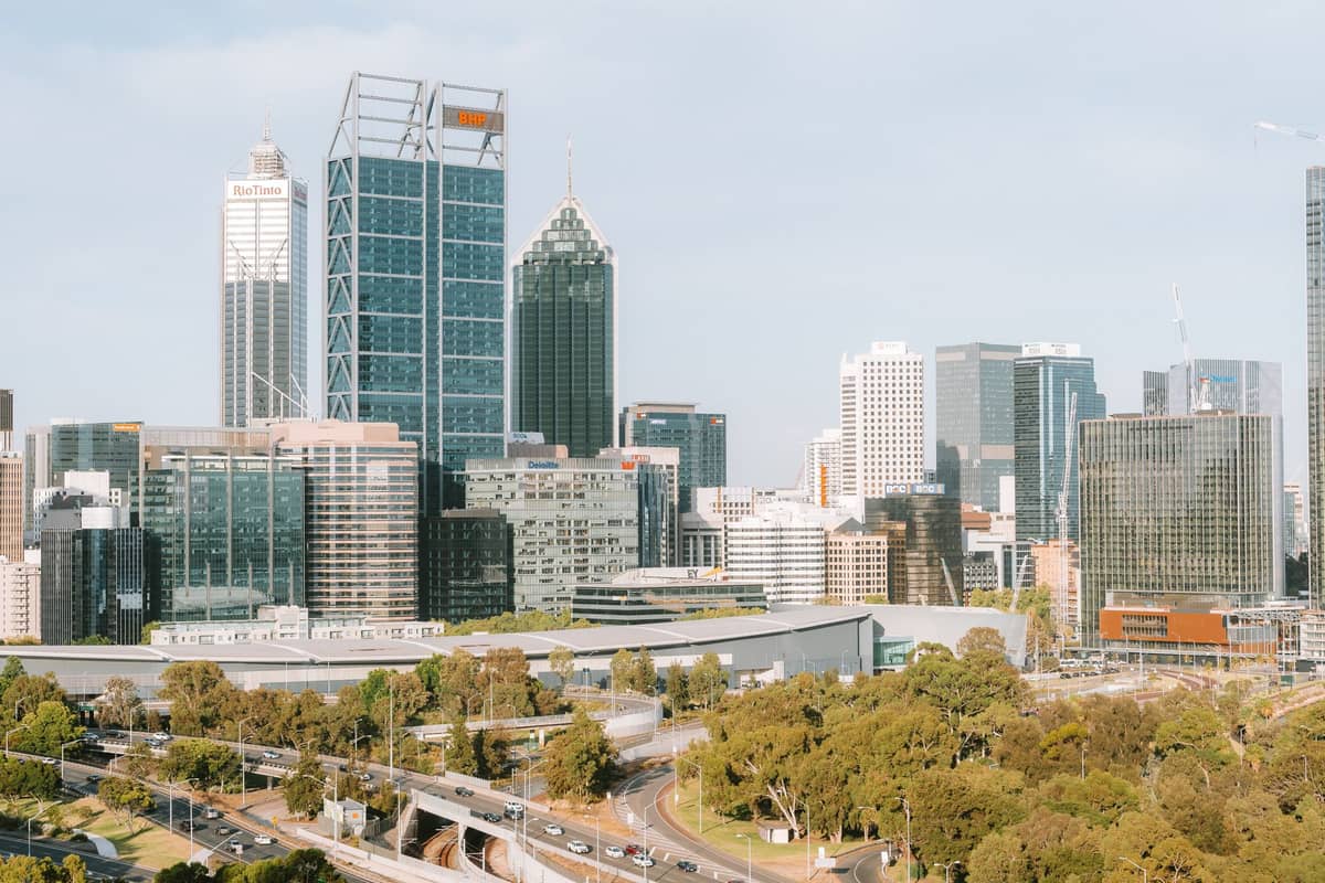 Weitläufiger Blick auf die Skyline des Perth CBD mit modernen Hochhaus-Bürotürmen, belebten Straßen und üppigem Grün im Vordergrund unter einem klaren Himmel.