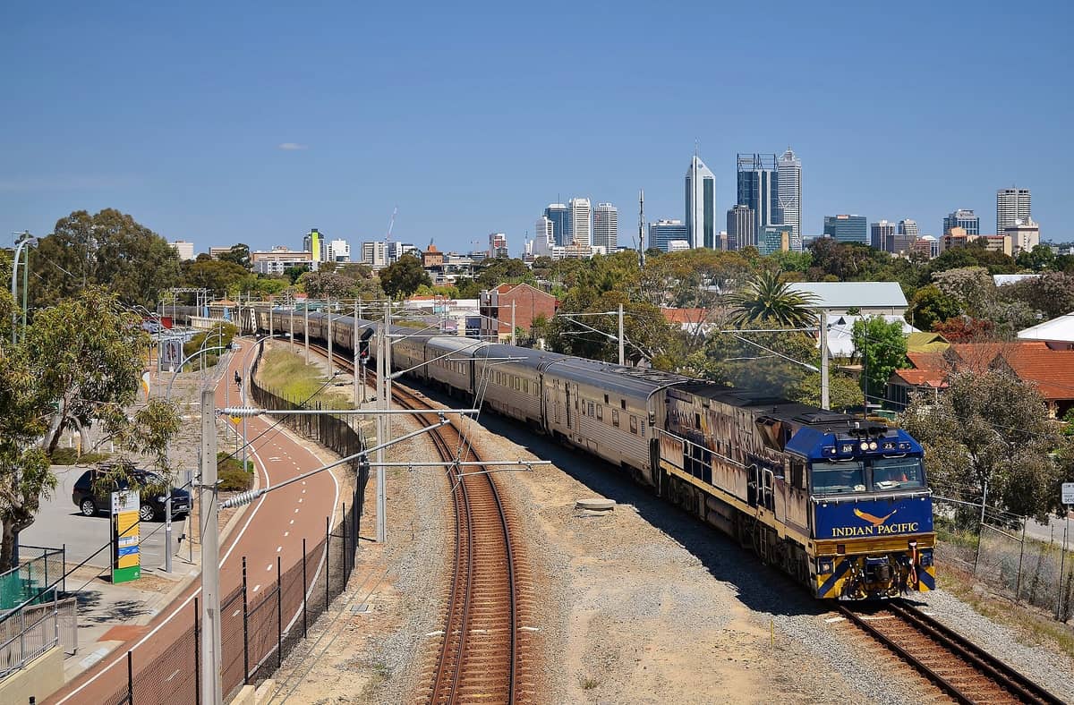 Đoàn tàu Indian Pacific chạy trên đường ray với đường chân trời của Perth ở phía sau dưới bầu trời xanh trong.