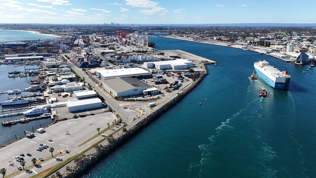 Luftaufnahme des Hafens von Fremantle mit Schiffen, Docks und der Stadtsilhouette im Hintergrund unter blauem Himmel.