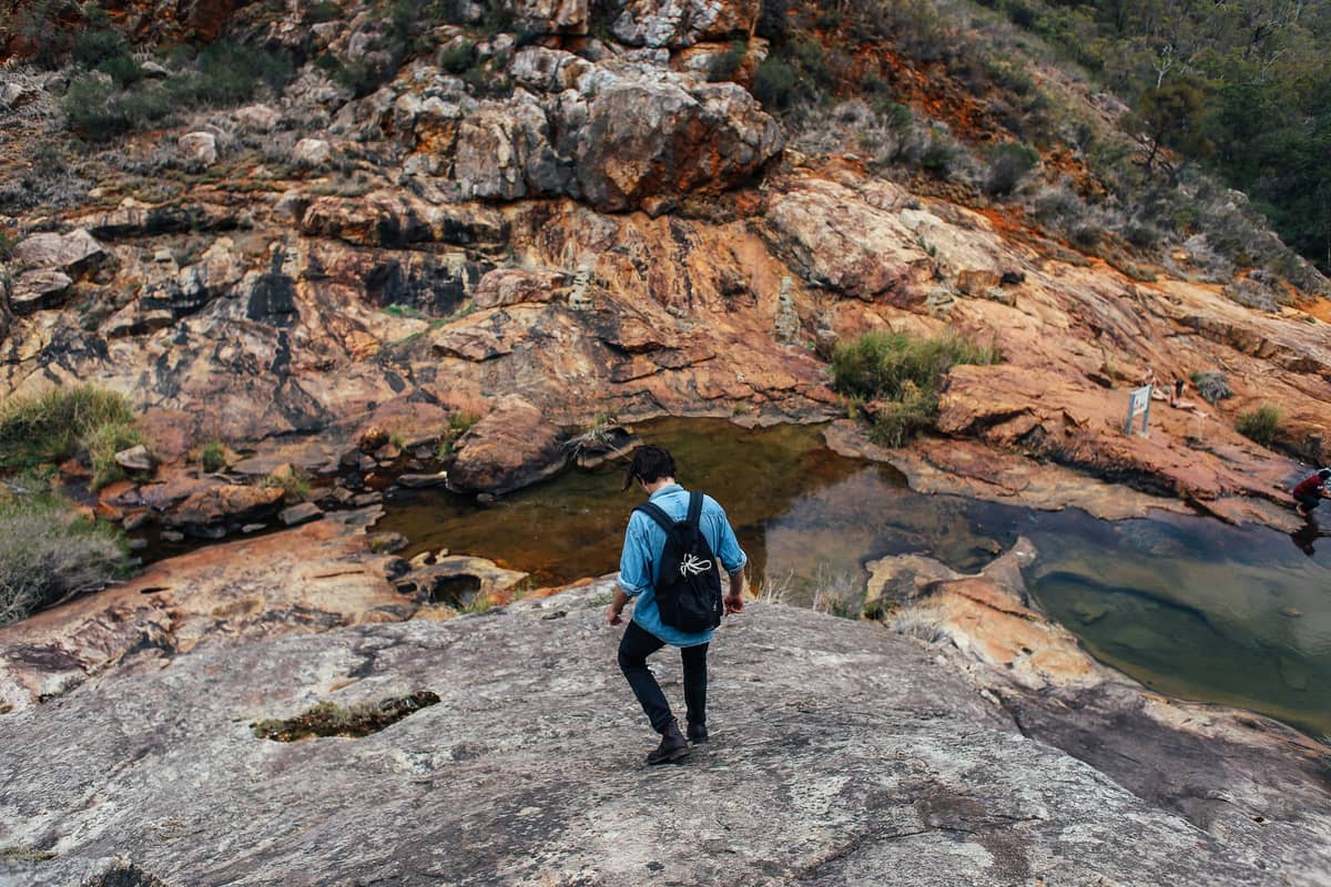 Person, die auf einem Felsvorsprung mit flachen Tümpeln und rauem Gelände läuft, typisch für die Landschaft des Perth Hills-Steilhangs.