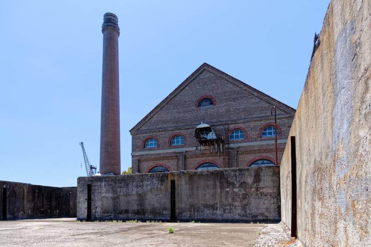 Historisches Backsteinkraftwerk mit einem hohen Schornstein unter klarem blauem Himmel, aufgenommen von einem offenen Betonhof in Perth.