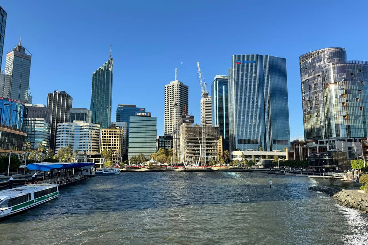 Widok na panoramę Perth z Elizabeth Quay — nowoczesne wieżowce, nadrzeczna promenada i łodzie na rzece Swan pod bezchmurnym błękitnym niebem.