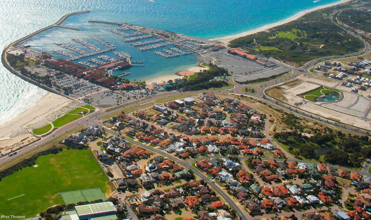 Aerial view of Hillarys Boat Harbour in Perth featuring marina, surrounding suburban area, parking lots, green spaces, and nearby Indian Ocean coastline.