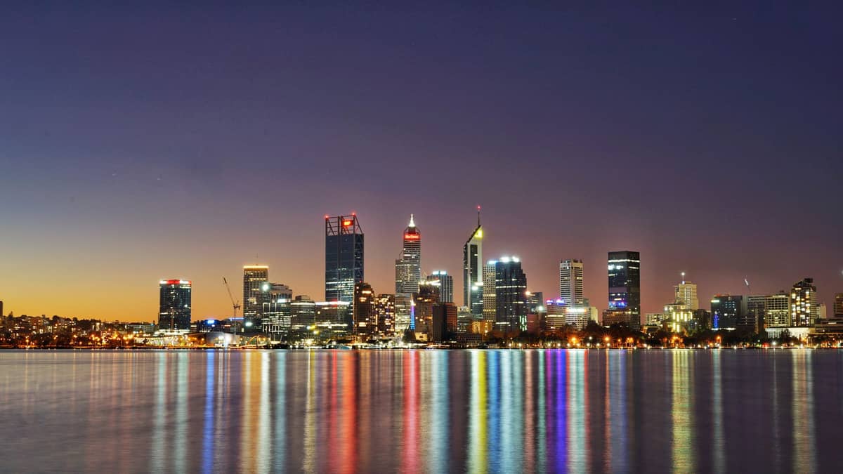 Panoramiczny widok na skyline Perth o zmierzchu — podświetlone wieżowce odbijają się w spokojnych wodach rzeki Swan.