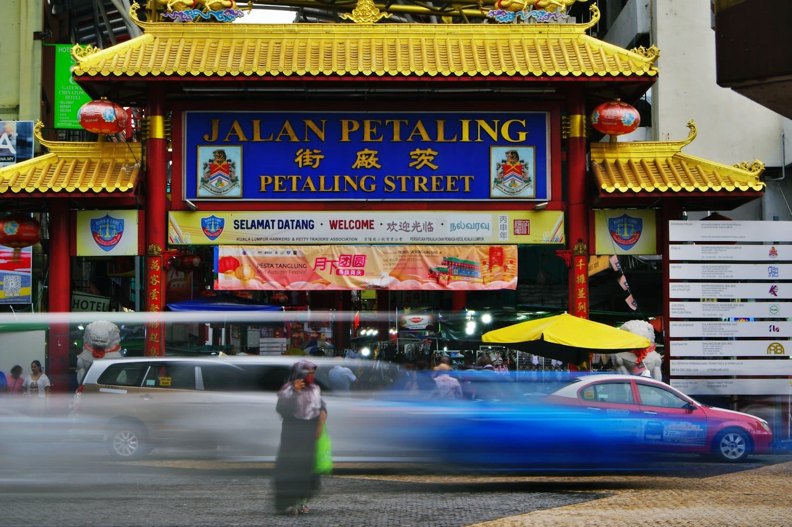 Bustling entrance to Petaling Street Market in Kuala Lumpur's Chinatown, framed by red lanterns and tiled arch.