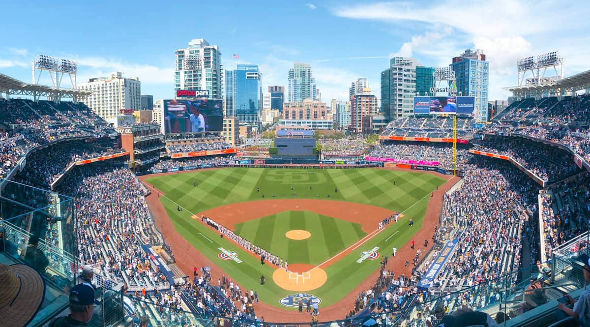 Weites Panorama des Petco Park, vollbesetzt mit Fans, im Hintergrund die Skyline der Innenstadt von San Diego bei strahlendem Sonnenschein.