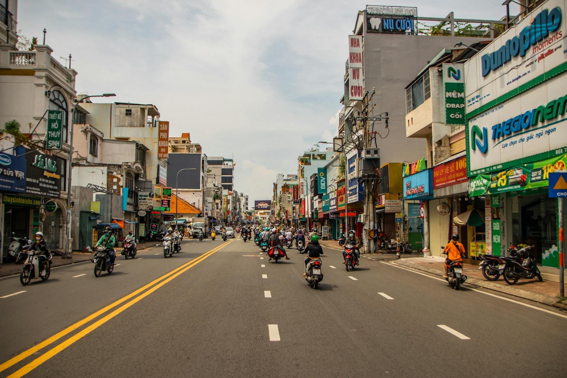 Calle animada del barrio mochilero de Phạm Ngũ Lão con motos, tiendas y carteles de colores a ambos lados bajo la luz del día.