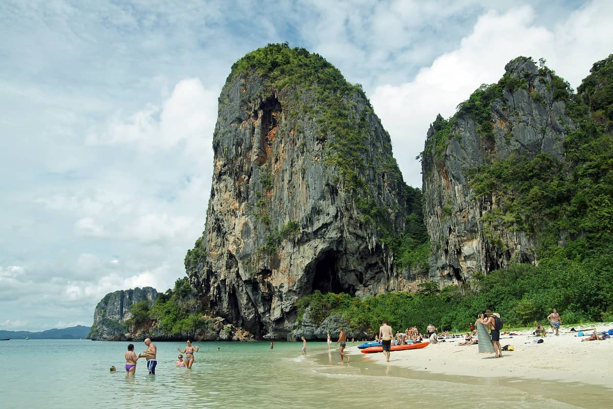Turistas nadan y descansan en la arena de la playa Phra Nang, con sus dramáticos acantilados de piedra caliza y exuberante vegetación verde al fondo.