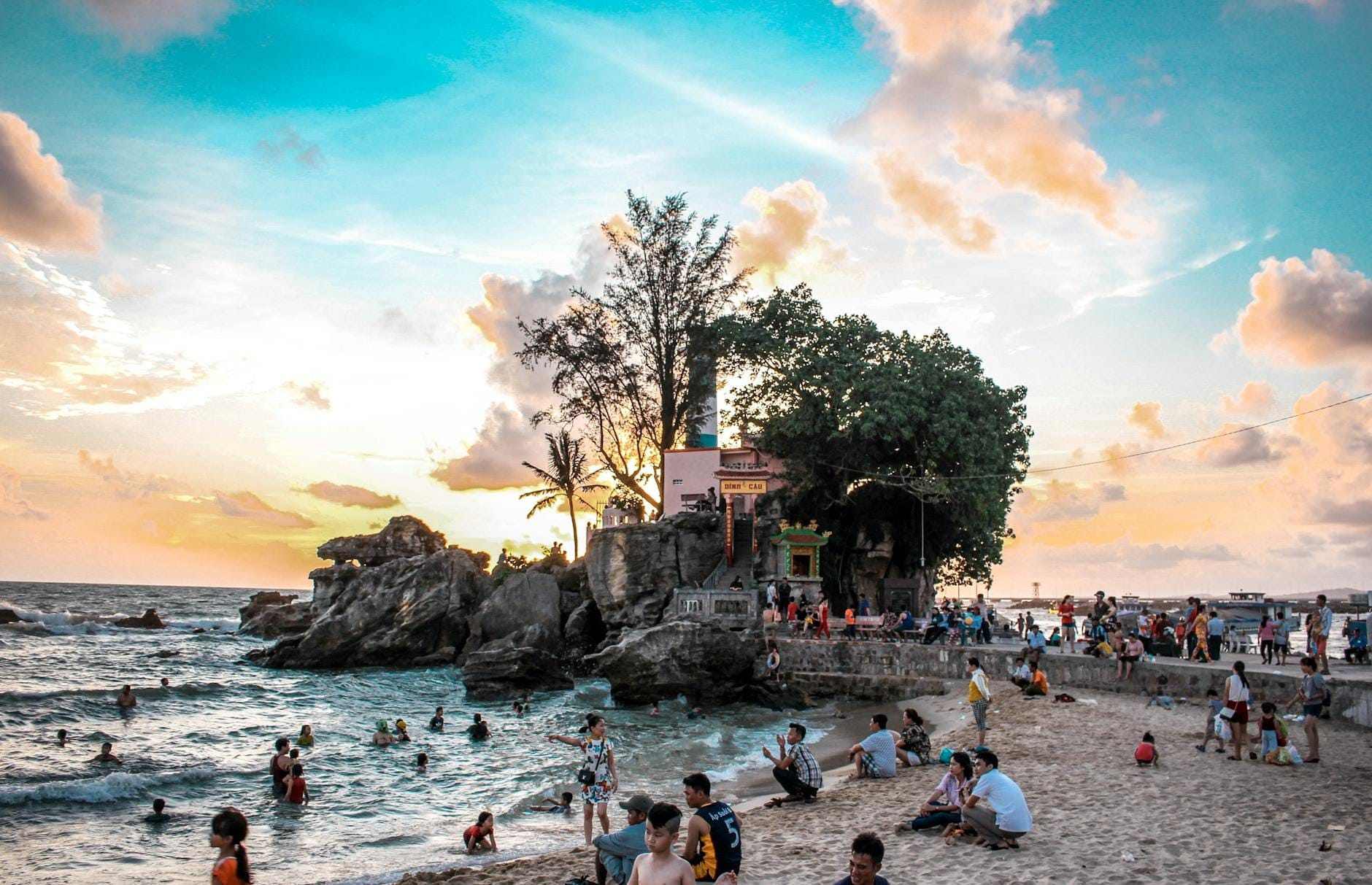 Praia de Phu Quoc ao pôr do sol com banhistas, costa rochosa e cenário de templo à beira-mar