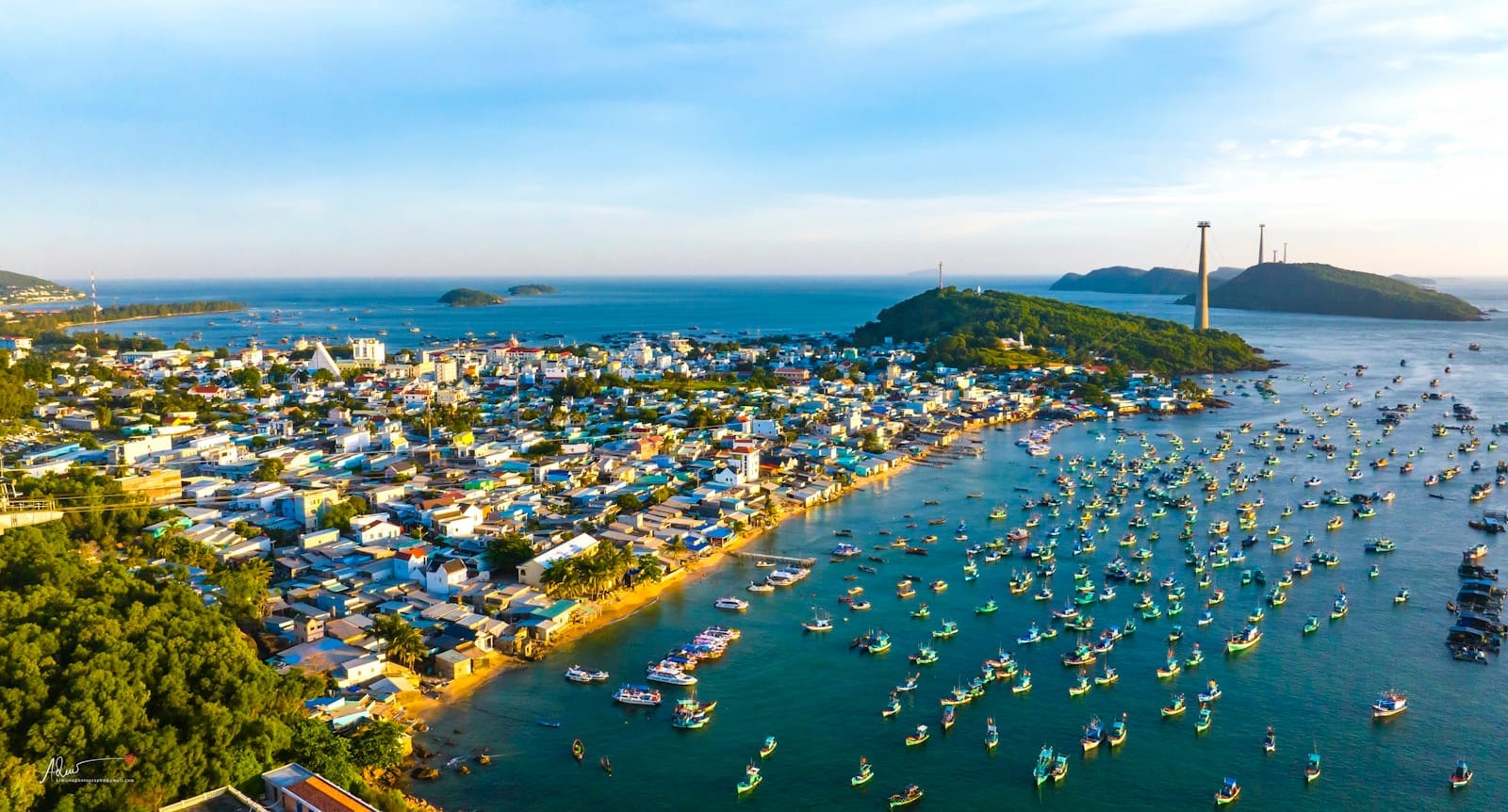 Luftaufnahme des An Thoi-Archipels auf Phu Quoc mit bunten Booten in der Bucht, einer Küstenstadt und grünen Inseln in der Ferne.
