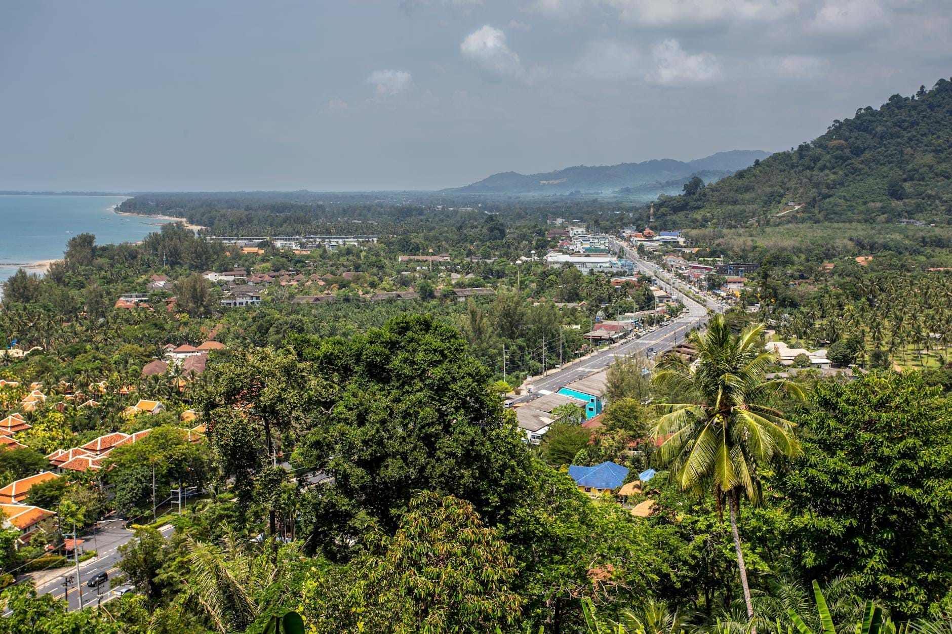 View from above of Kata or Karon beach area, showing lush hillsides, a long sandy beach, town, and the coastline stretching into the distance.