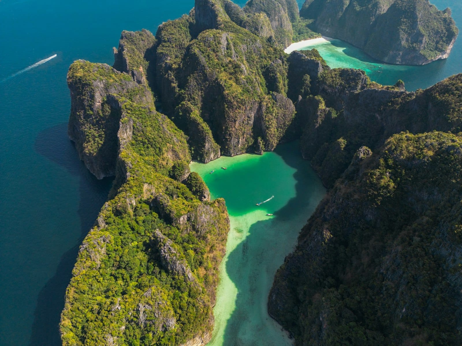 Aerial view of dramatic limestone islands and turquoise lagoon waters, typical of the Phi Phi islands near Phuket, with boats in the bay.