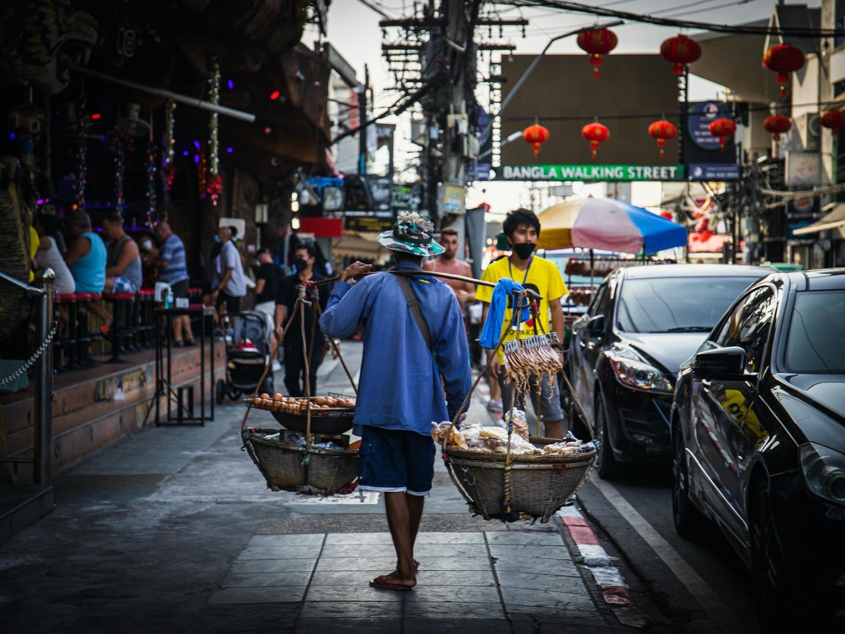 A busy street scene in Phuket’s Bangla Road at dusk with a street vendor carrying food and the Bangla Walking Street sign overhead.