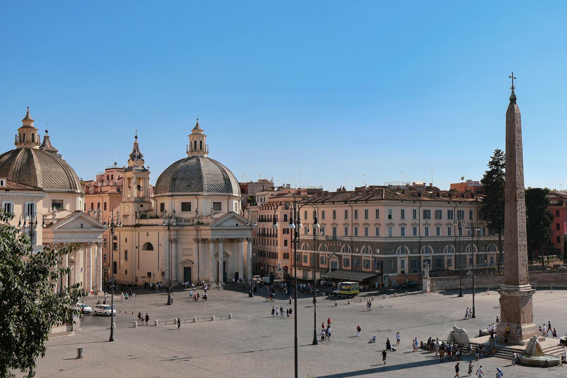 Wide view of Piazza del Popolo in Rome featuring the central Egyptian obelisk, twin Baroque churches, and the sweeping oval square on a sunny day.