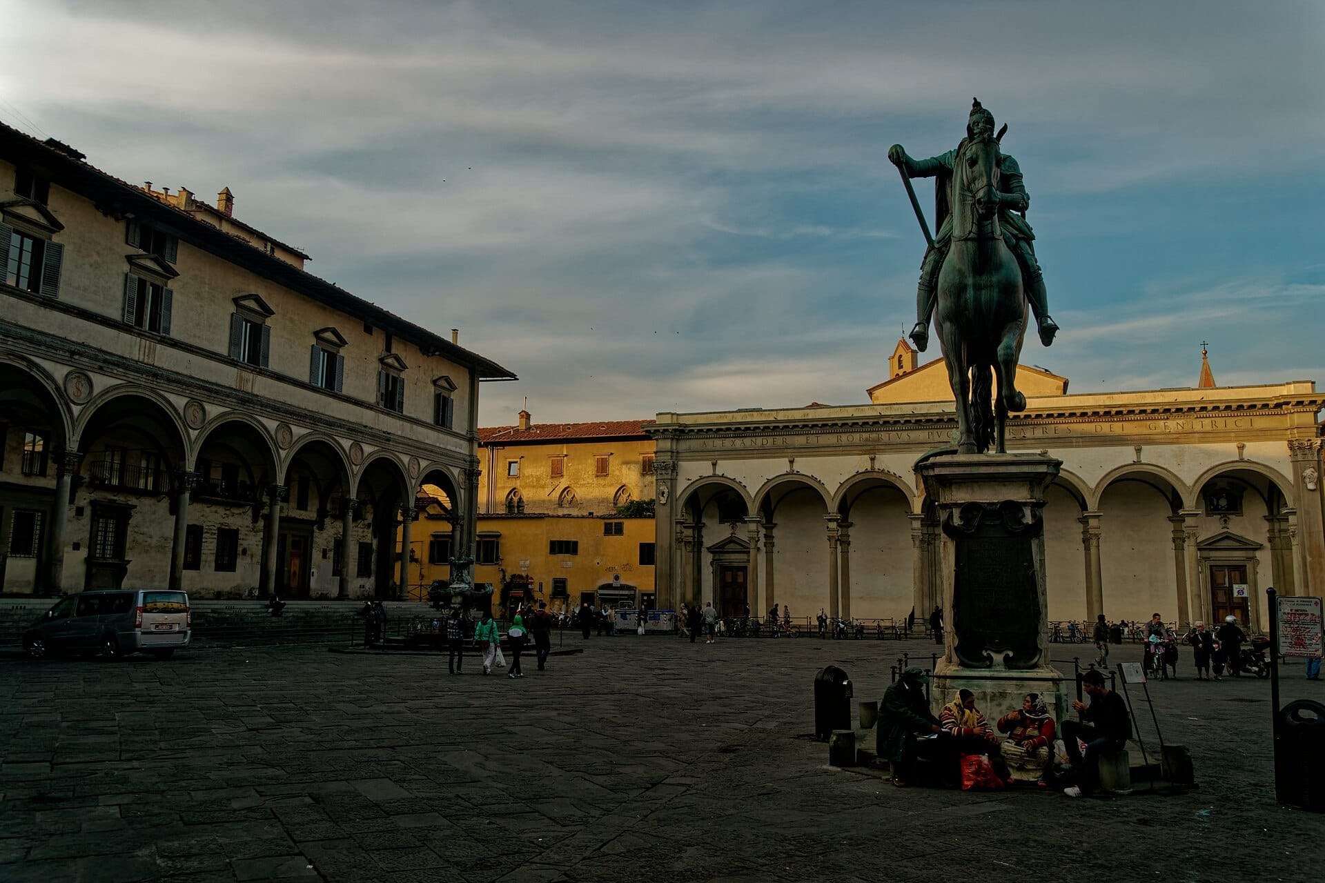 Piazza della Santissima Annunziata ในเมืองฟลอเรนซ์ พร้อมอาคารยุคเรอเนสซองส์แบบมีระเบียงโค้ง รูปปั้นทหารม้าสำริดของตระกูล Medici และนักท่องเที่ยวที่เดินข้ามจัตุรัสในยามพลบค่ำ