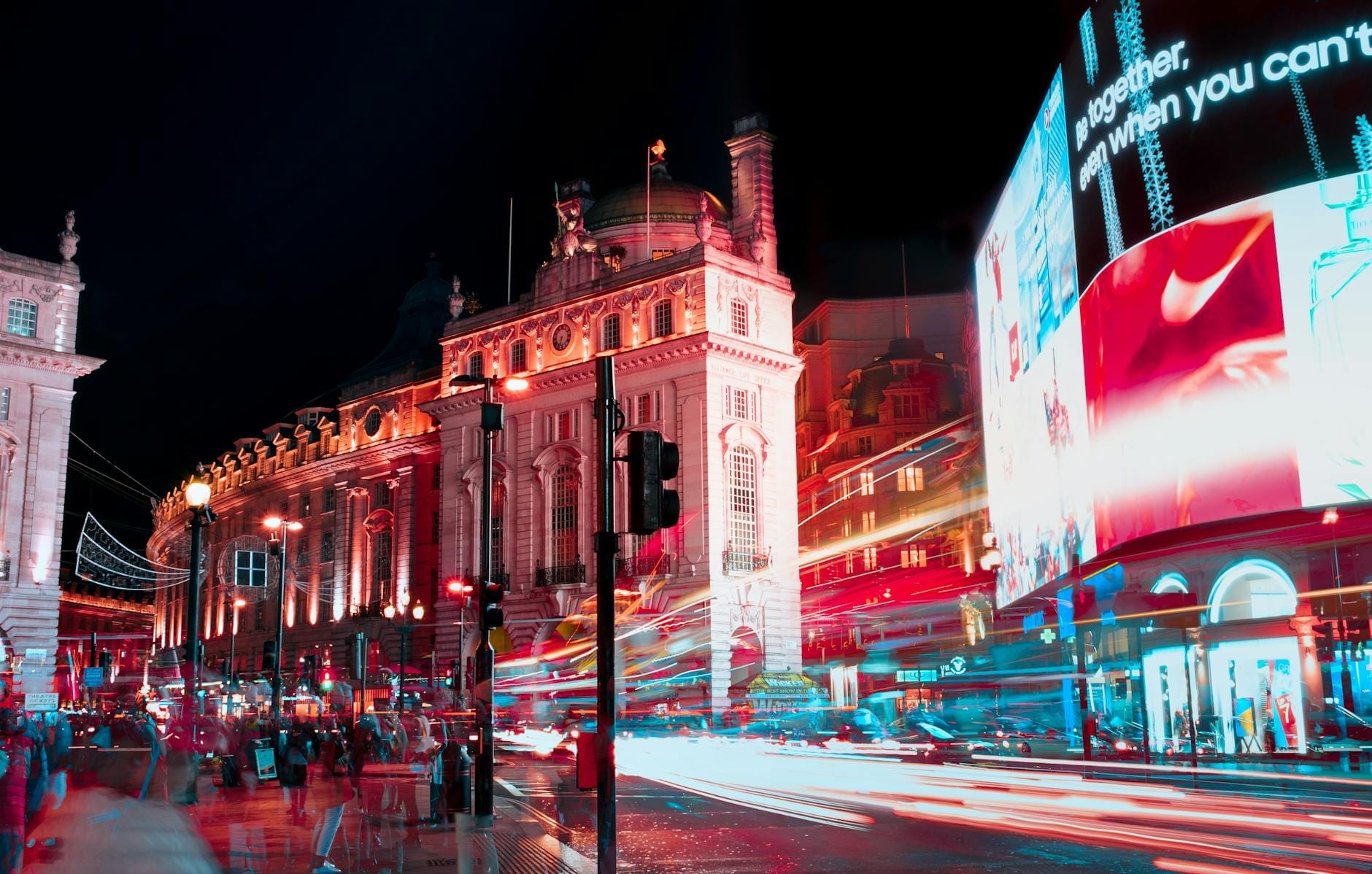 Piccadilly Circus di notte con luci al neon vivaci, edifici illuminati, scie luminose del traffico e folla di persone che catturano il cuore pulsante di Londra.