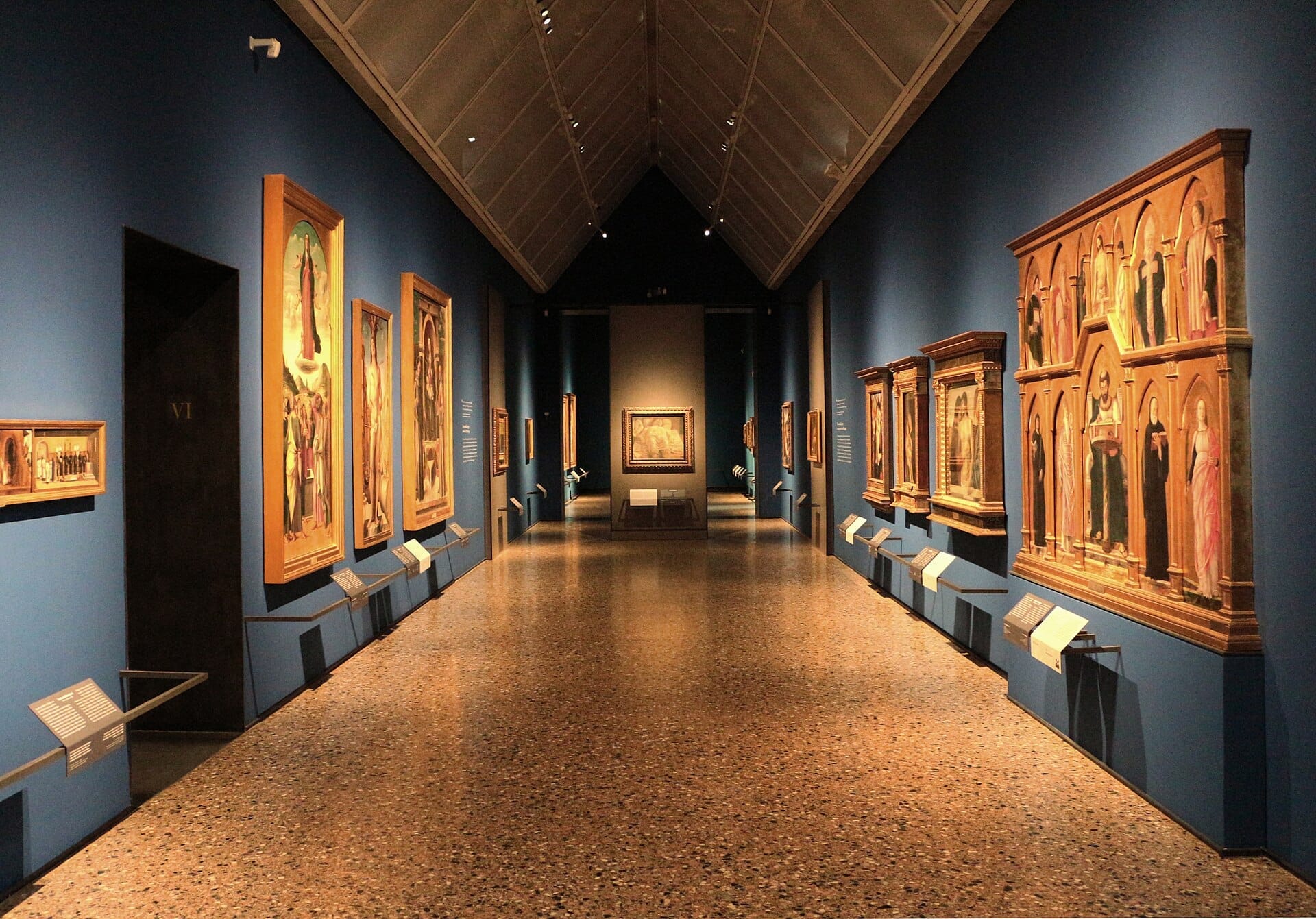 Vista ampia di una sala della Pinacoteca di Brera, Milano, con dipinti rinascimentali esposti su pareti blu intenso sotto una luce soffusa.