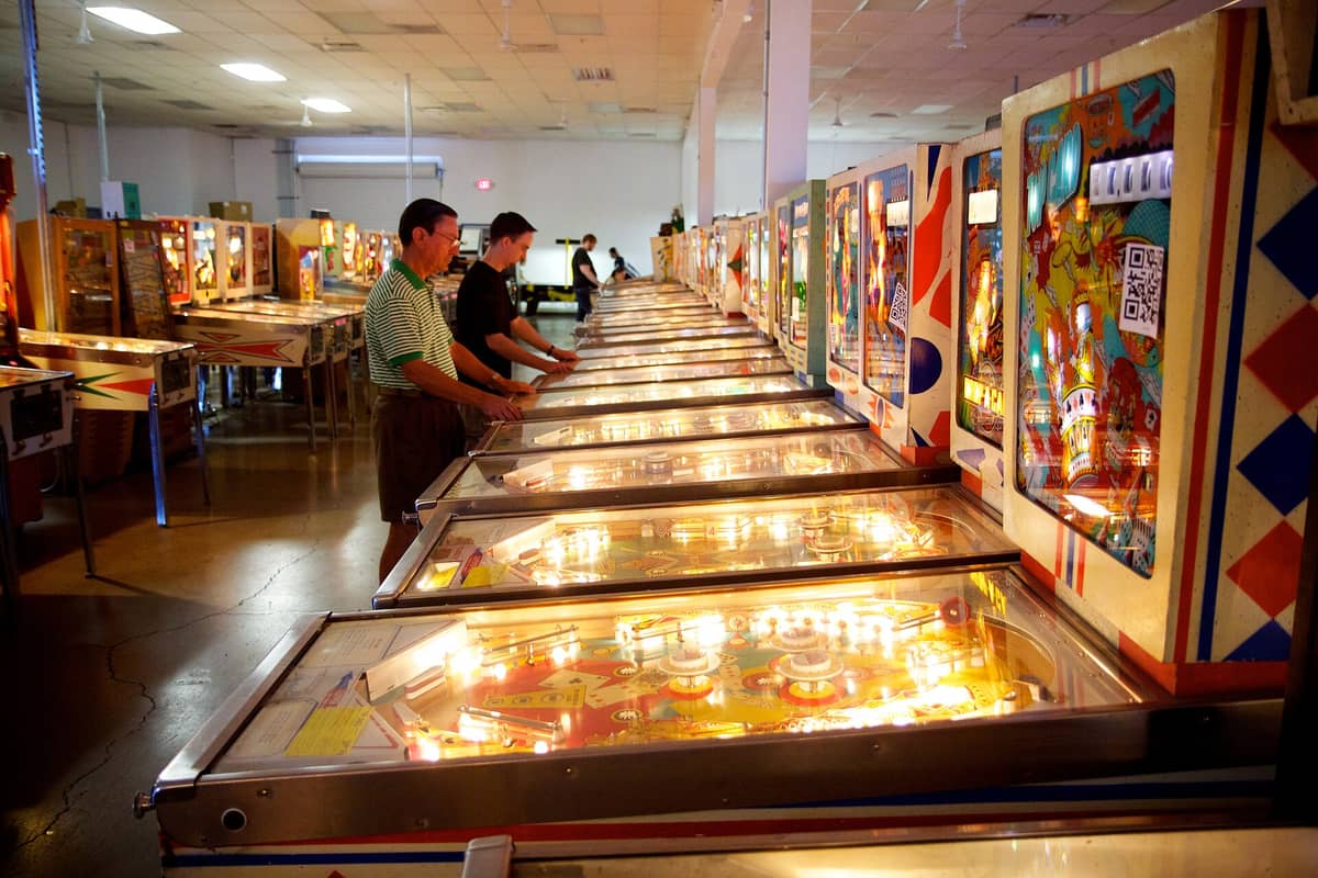 Deretan mesin pinball vintage di dalam Pinball Hall of Fame Las Vegas, dengan orang-orang bermain di ruang arcade yang terang benderang.