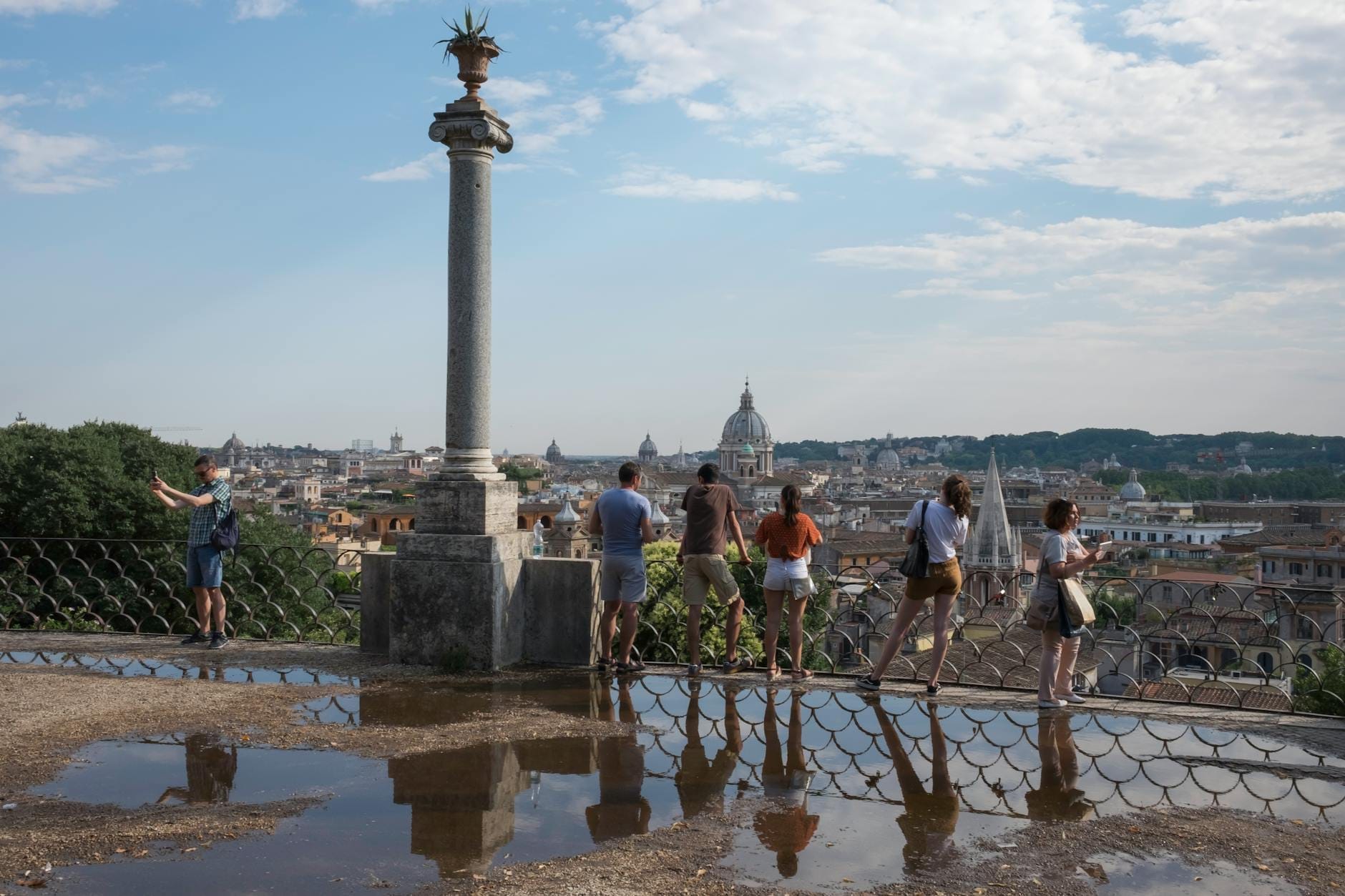 Visitors enjoying the panoramic view from Pincio Terrace over Rome’s rooftops, with the dome of St. Peter’s Basilica visible in the distance under a blue sky.
