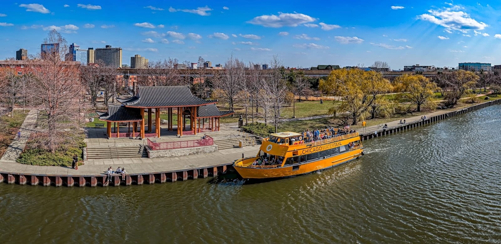 Vista panoramica luminosa del padiglione sul fiume del Ping Tom Memorial Park, con un water taxi giallo ormeggiato lungo il Chicago River in una giornata di sole.