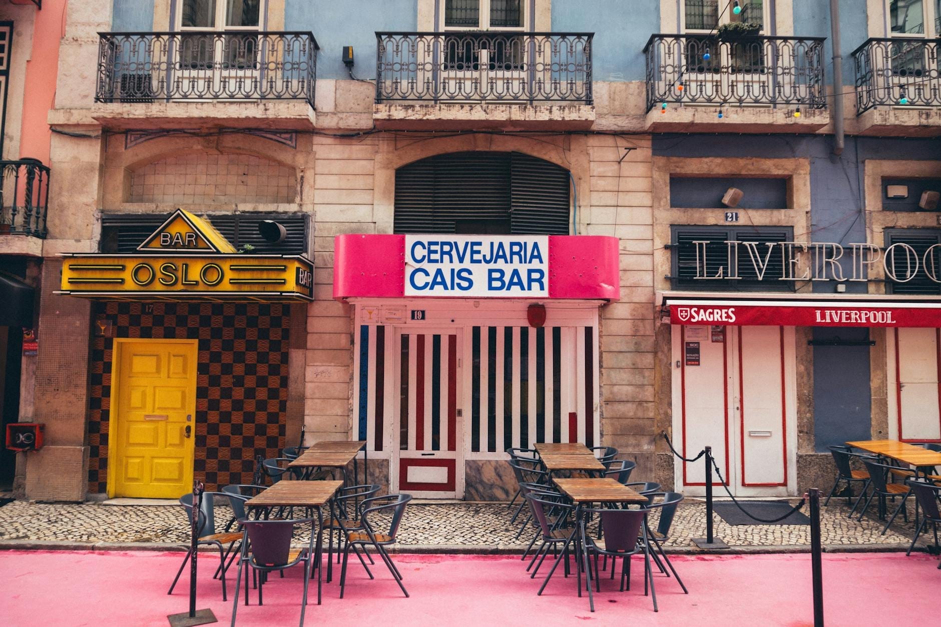 Le facciate colorate dei bar vintage con tavolini all'aperto lungo il selciato rosa della Rua Nova do Carvalho, la famosa Pink Street di Lisbona, di giorno.