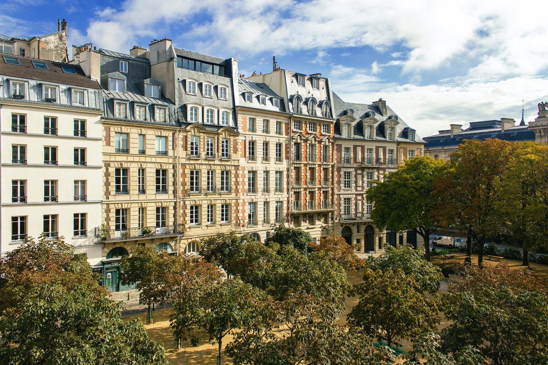 Vista dall'alto di Place Dauphine con i platani rigogliosi, i classici edifici parigini del XVII secolo e un cielo blu, che cattura il fascino quieto della piazza.