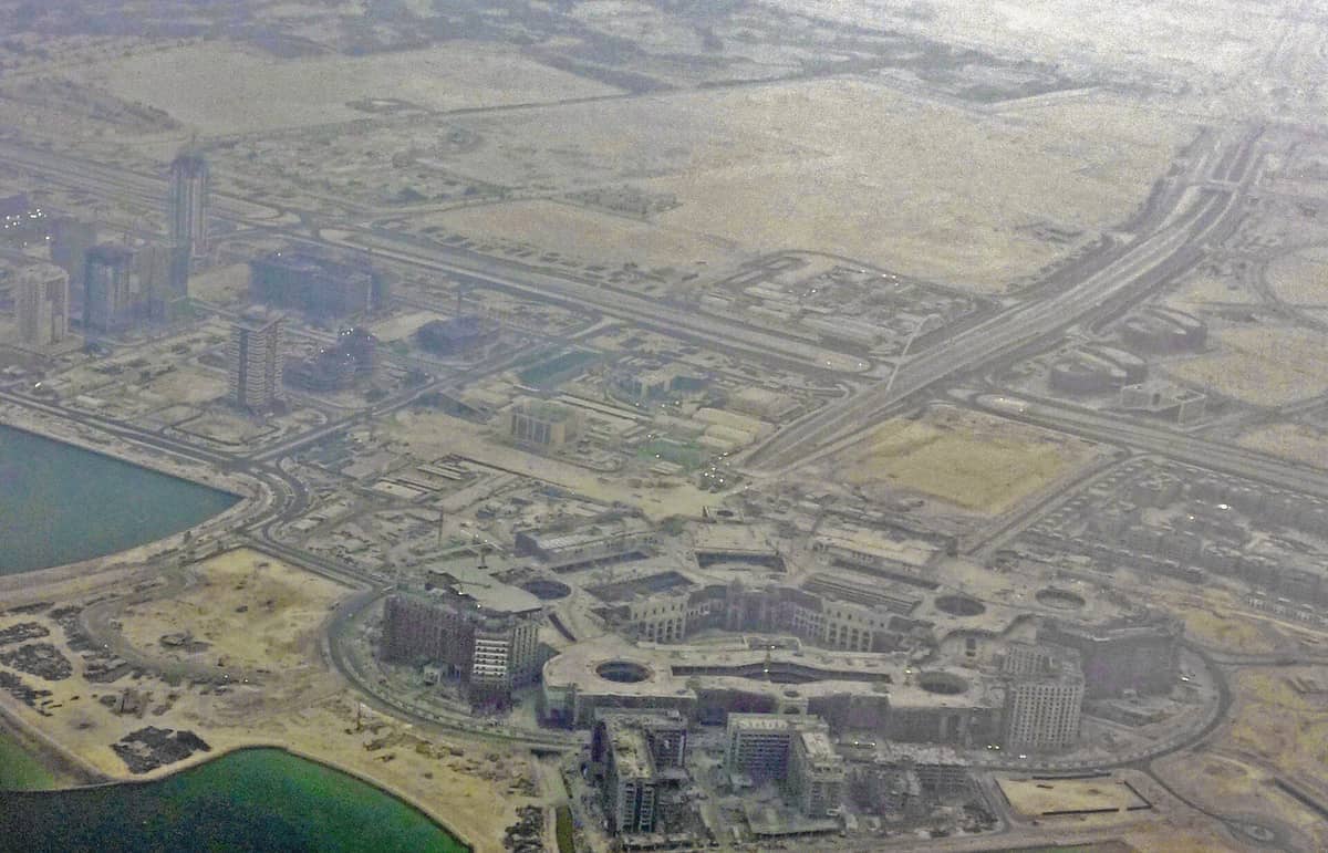 Luftaufnahme des Place Vendôme Mall in Lusail, Katar, umgeben von modernen Gebäuden, Autobahnen, Kanälen und sandiger Wüstenlandschaft.