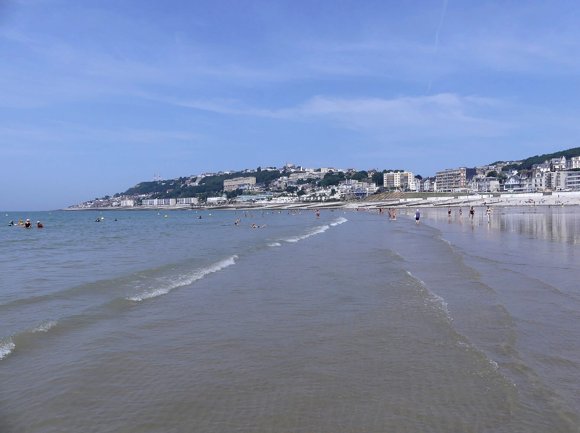วิวของ Plage de Sainte-Adresse พร้อมคลื่นเบาๆ ชายหาดทราย นักท่องเที่ยวที่กระจายอยู่ และอาคารของเมืองที่ตั้งเรียงรายบนไหล่เขา