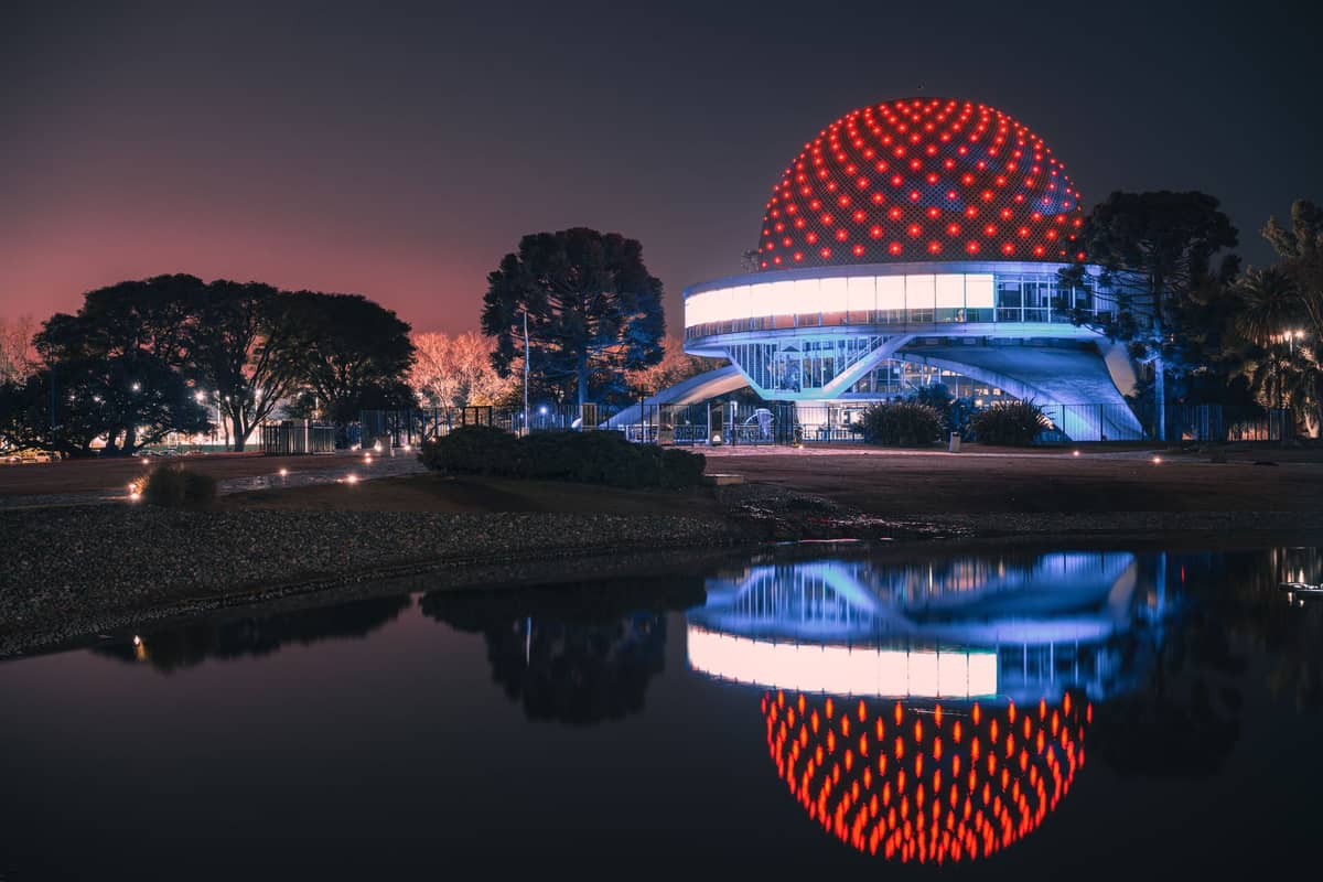 Planetario Galileo Galilei ยามค่ำ โดมเรืองแสงสะท้อนในทะเลสาบ ริมต้นไม้ในสวนปาแลร์โมแห่งบัวโนสไอเรส