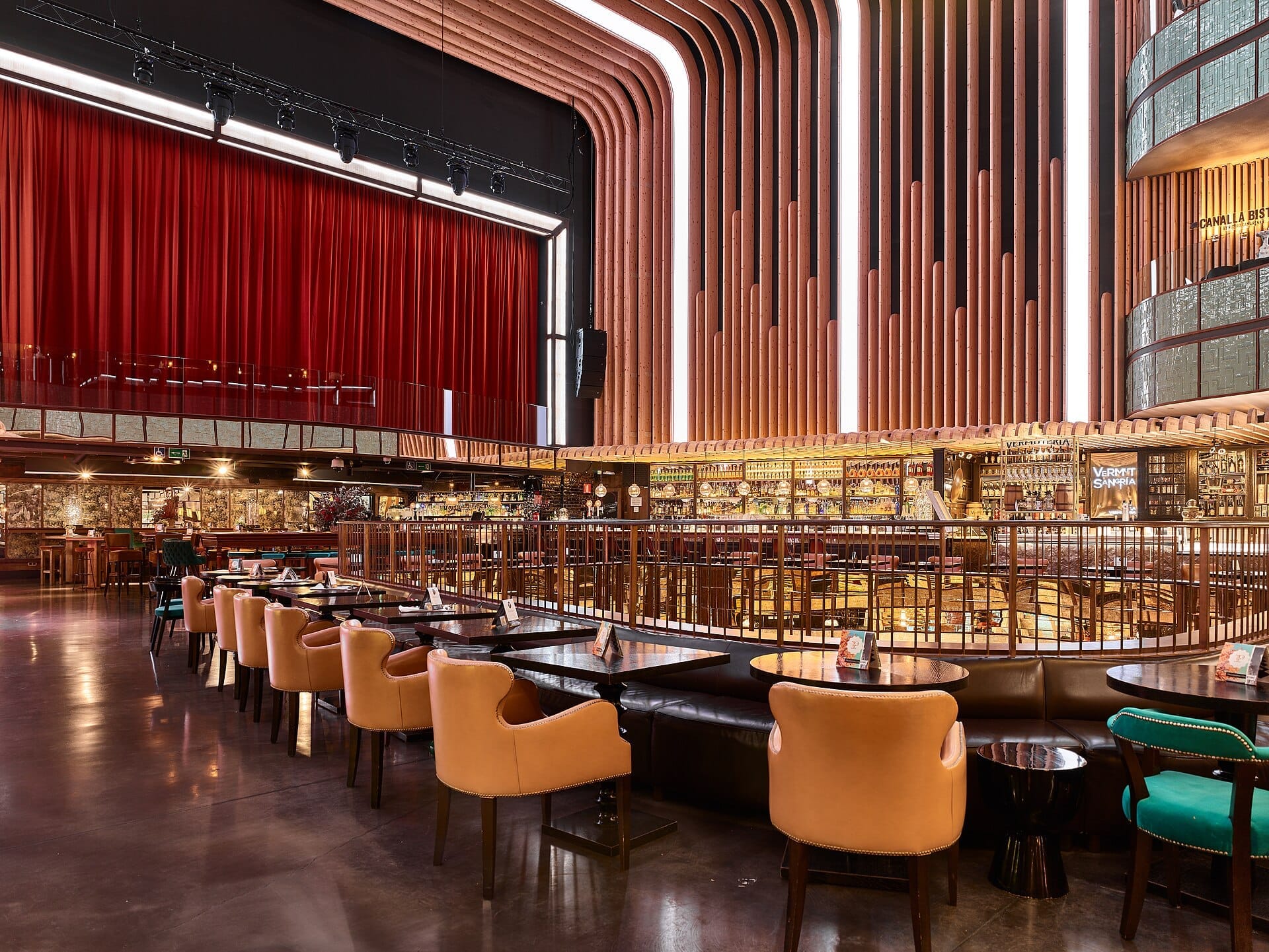 Vista ampia del mercato gastronomico Platea Madrid con illuminazione moderna, dettagli curvi in legno, sedie in pelle e un sipario rosso in un ex cinema.