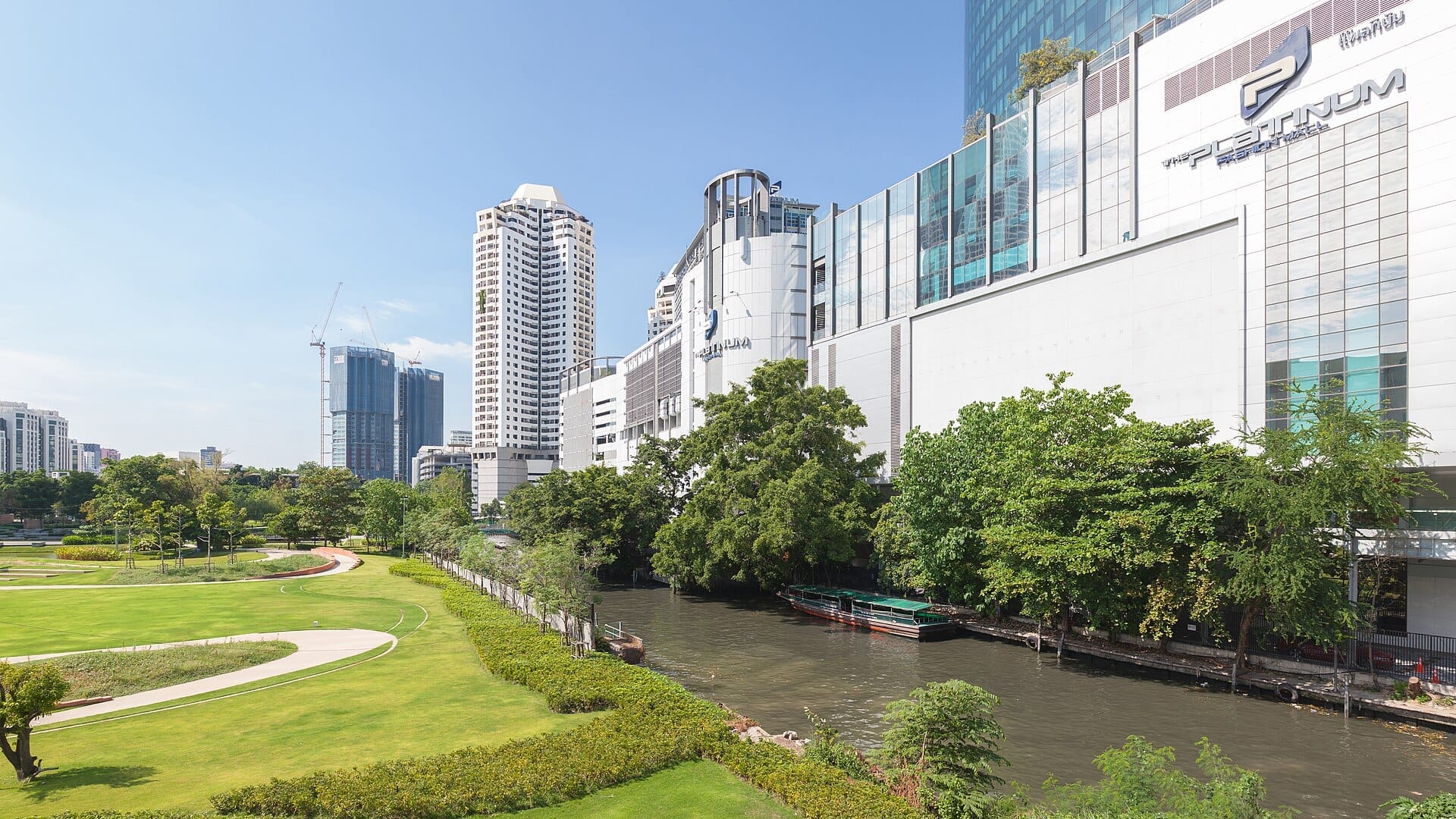 Il Platinum Fashion Mall di Bangkok visto dal canale, con parco, alberi e lo skyline di Pratunam