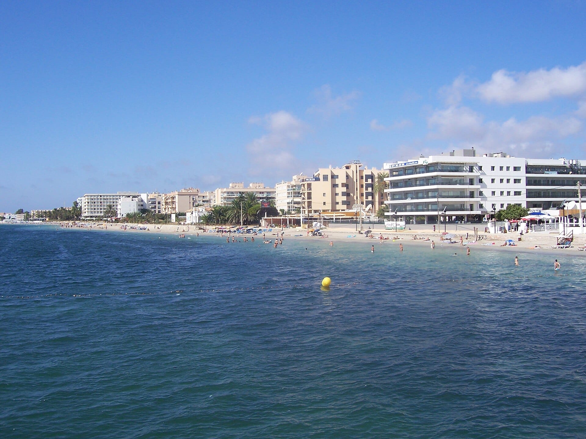 วิวของ Playa d'en Bossa พร้อมโรงแรมริมชายหาดสมัยใหม่ หาดทราย นักอาบแดด และน้ำสีฟ้าใสใต้ท้องฟ้าสดใส