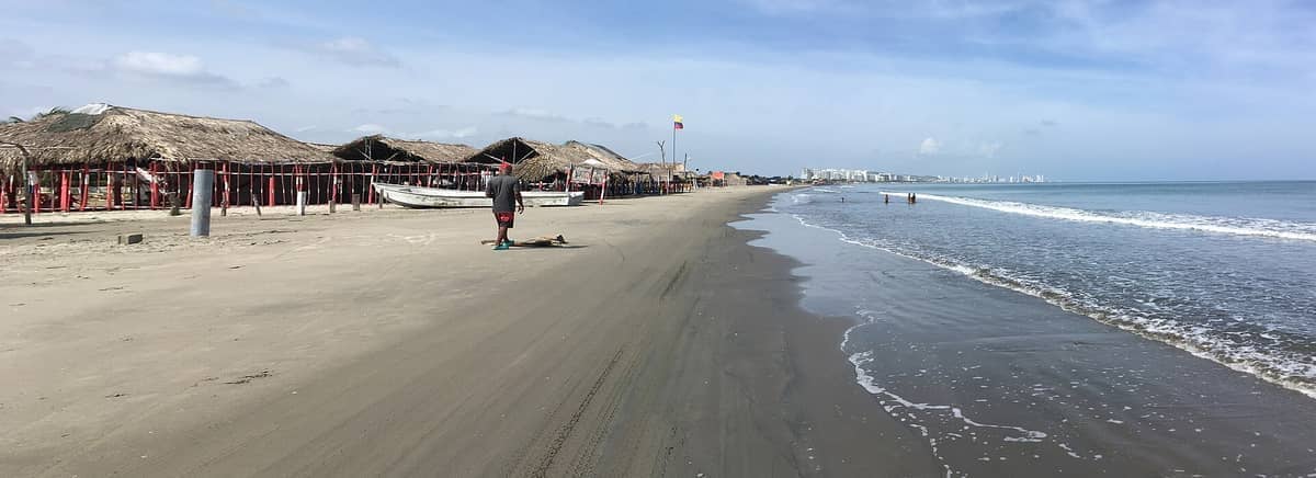 Wide sandy shoreline at Playa Azul La Boquilla with rustic beach shacks, fishing boats, gentle surf, and local people enjoying the ocean.