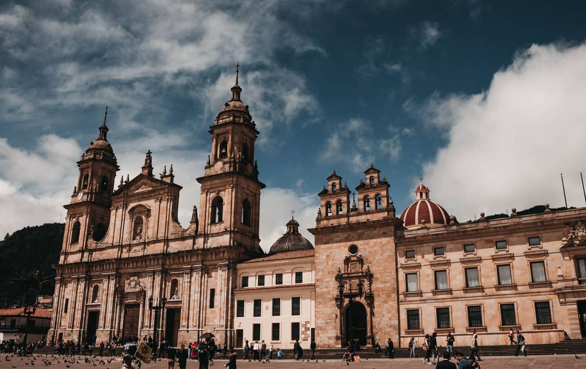Wide-angle view of Plaza de Bolívar in Bogotá featuring the cathedral and historic colonial buildings under a partly cloudy sky with people in the square.