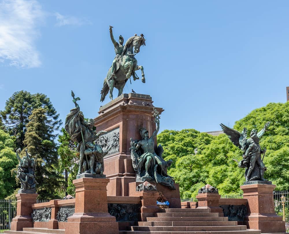 อนุสาวรีย์ทหารม้าสัมฤทธิ์ของนายพล San Martín ที่ Plaza San Martín กรุง Buenos Aires ล้อมรอบด้วยรูปปั้นที่มีรายละเอียดและต้นไม้เขียวขจีใต้ท้องฟ้าแจ่มใส