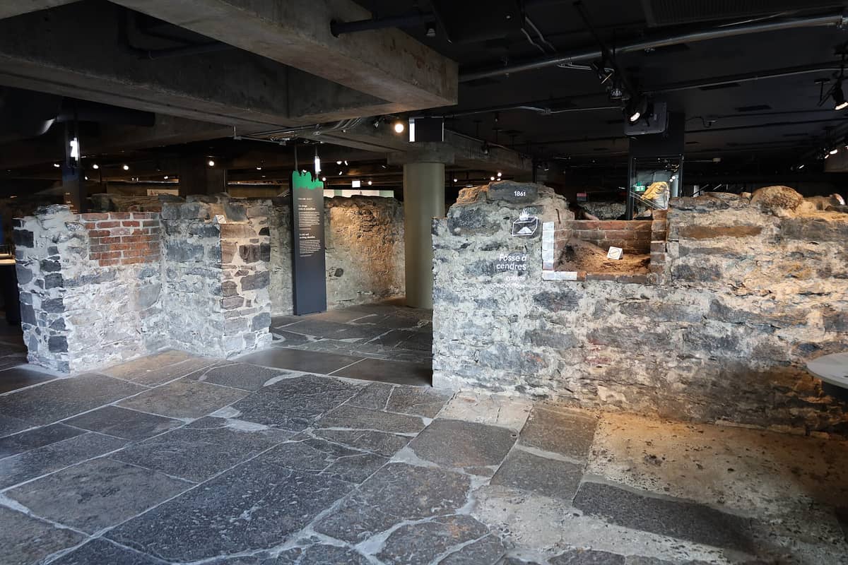 Innenansicht des Pointe-à-Callière Museums mit freigelegten archäologischen Steinruinen und städtischen Schichten unter einem modernen Gebäude mit Erläuterungstafeln.