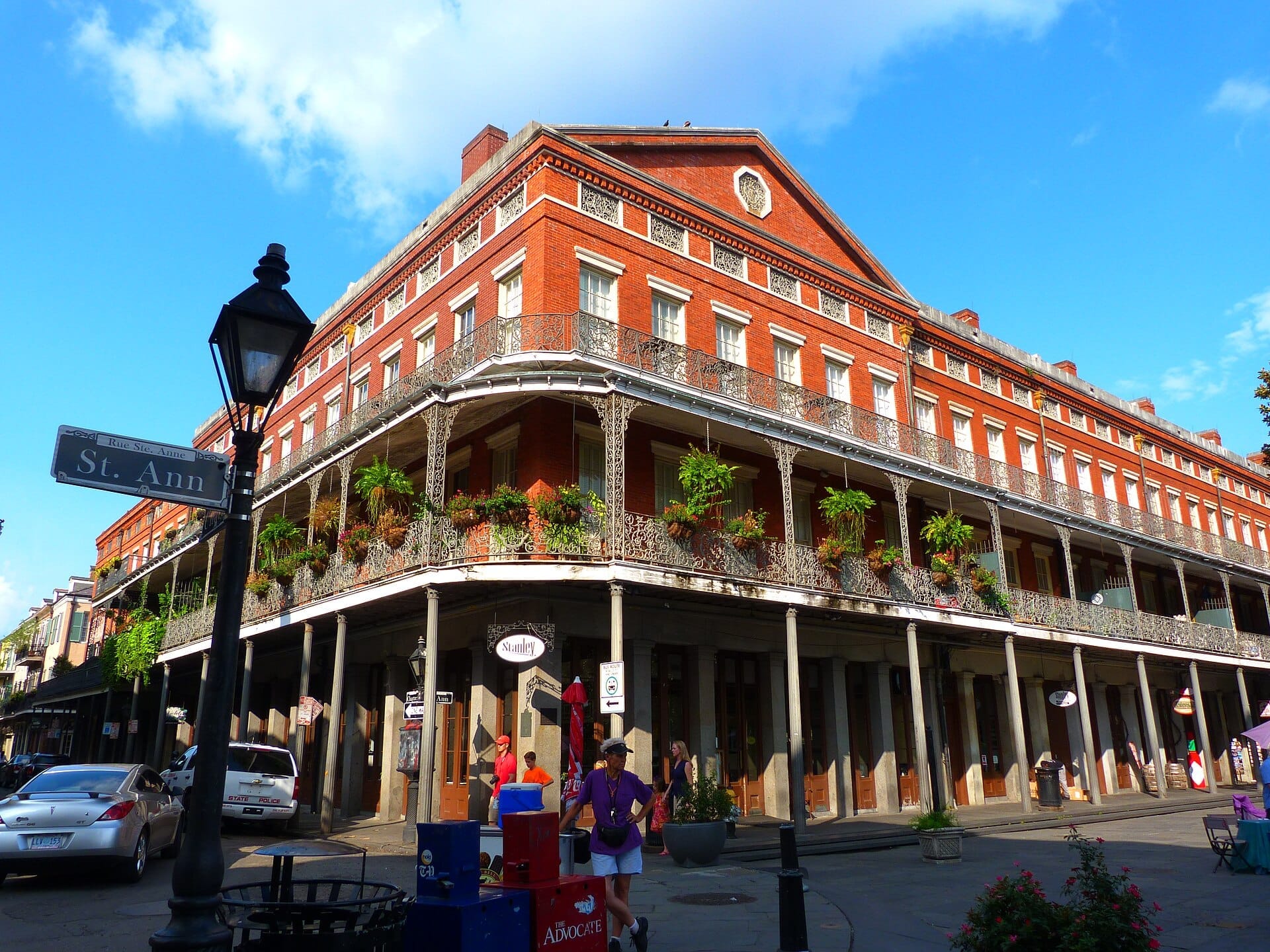 Gli edifici Pontalba a New Orleans, con facciata in mattoni rossi, balconi in ghisa, cartello stradale, auto parcheggiate e pedoni sotto un cielo azzurro.