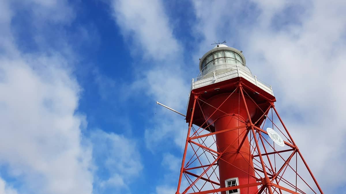 Close-up view of the red cast-iron Port Adelaide Lighthouse against a partly cloudy blue sky, highlighting its historic maritime structure.
