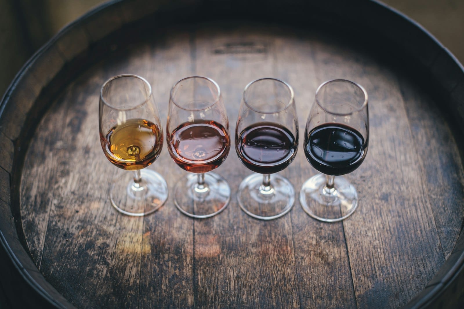 Quatro taças de vinho do Porto em cores diferentes dispostas sobre um barril de madeira, representando uma degustação em Porto.