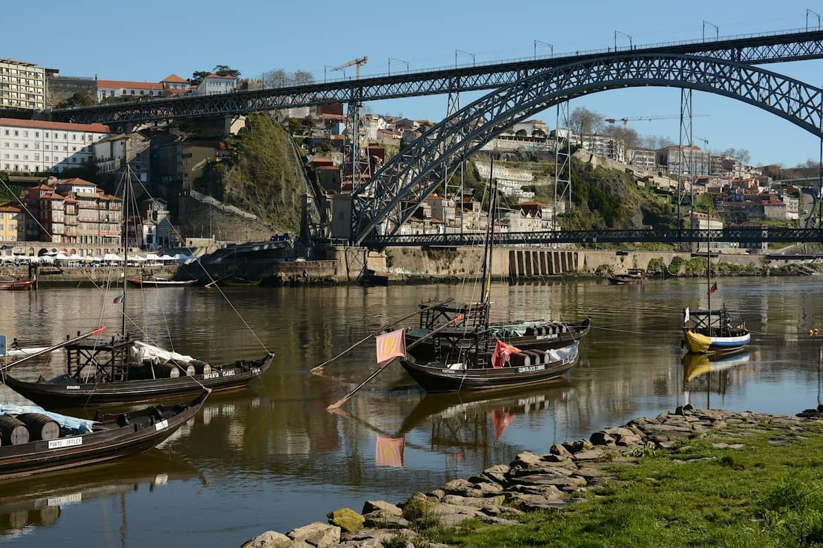 Łodzie rabelo na rzece Douro przed mostem Dom Luís I, z piwnicami win w Gaia i budynkami Porto w tle.