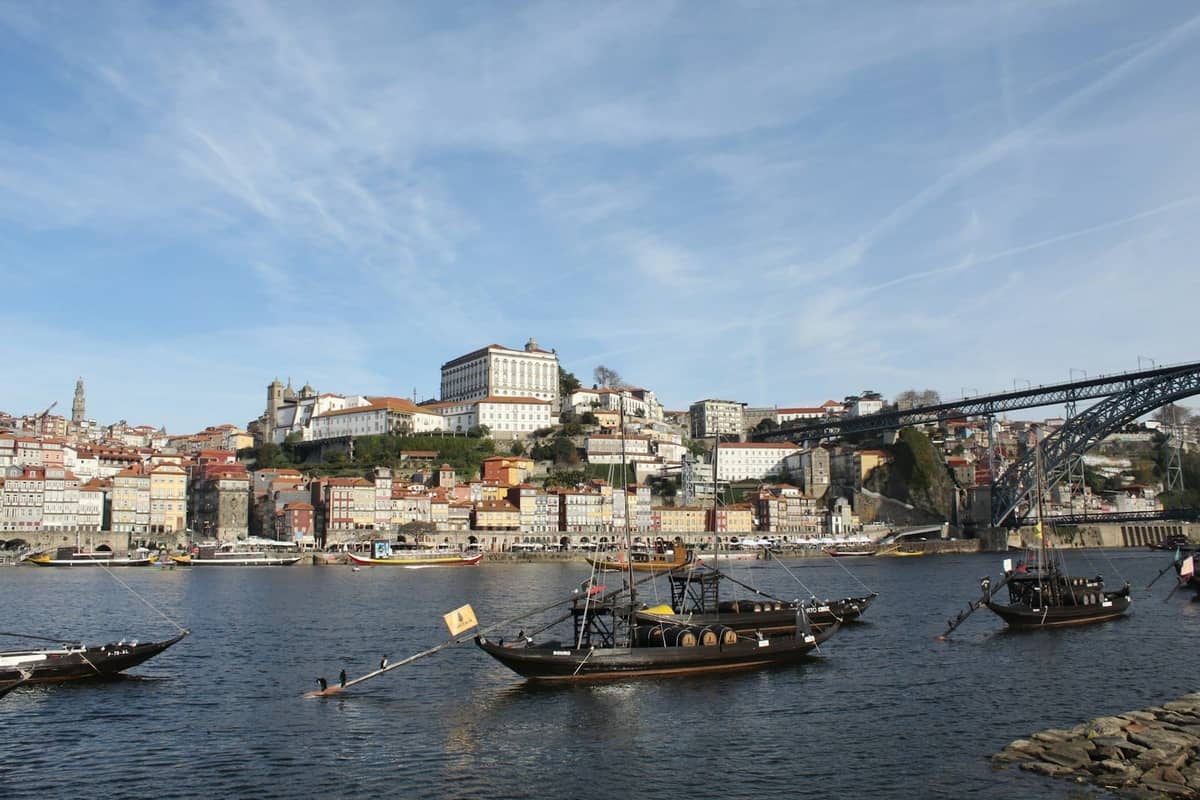 Łodzie rabelo z beczkami wina na rzece Douro w Porto, z historycznym miastem i słynnymi budynkami na zboczach wzgórz w tle.