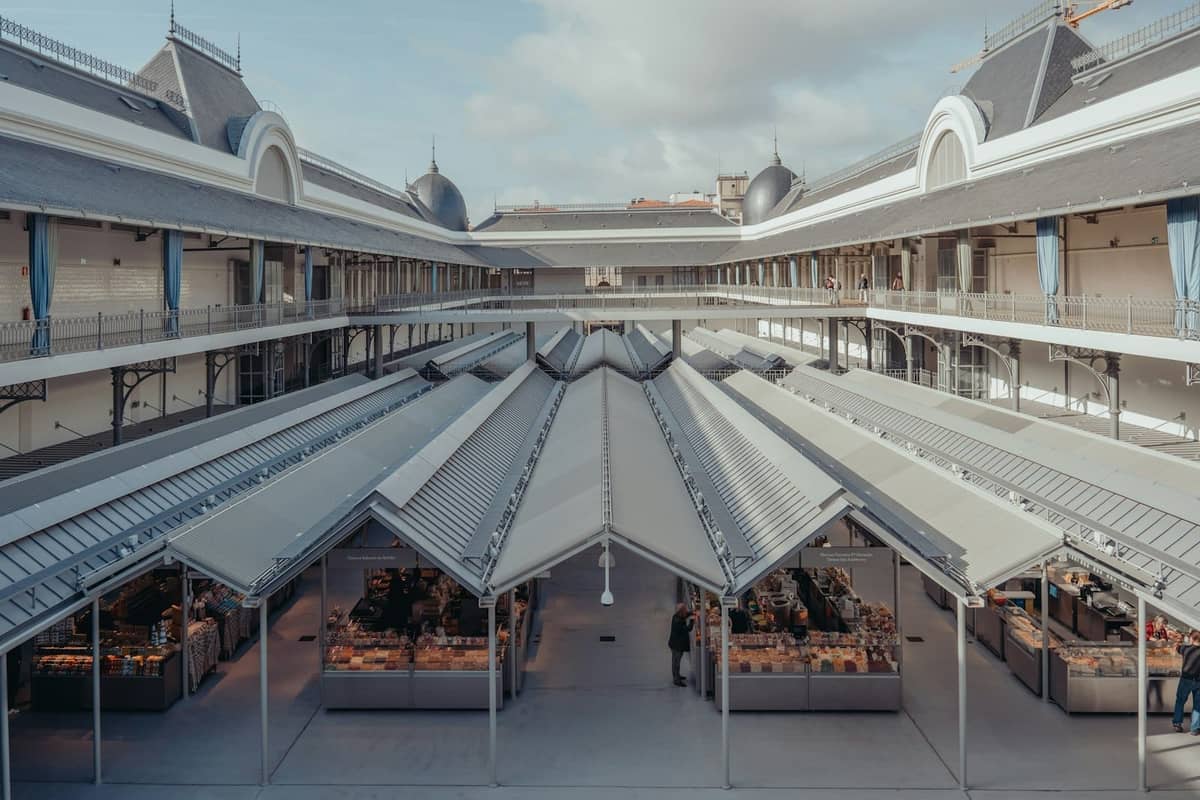 Vista ampla do interior renovado do Mercado do Bolhão com bancas iluminadas, teto de vidro e andares superiores ao redor, no Porto, Portugal.
