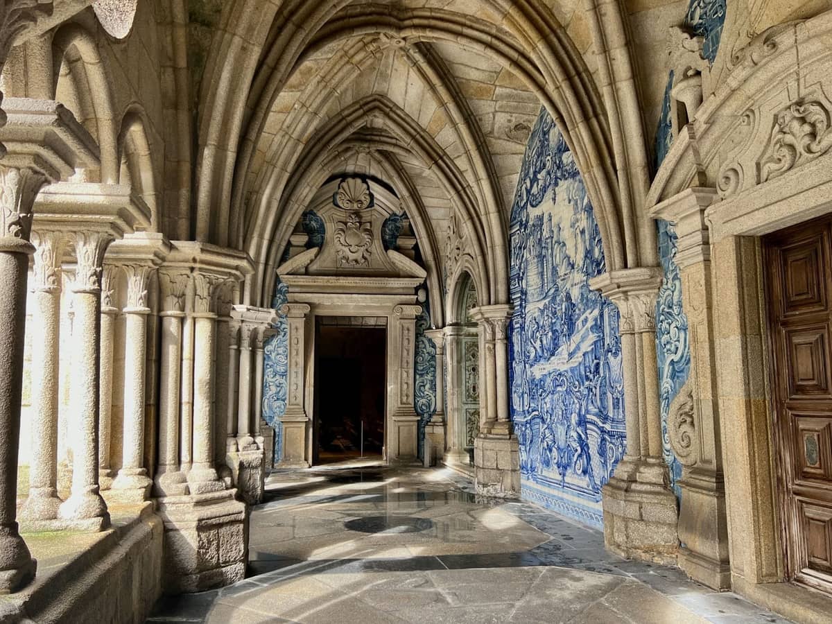Gewölbter Steinkorridor mit blauen und weißen Azulejo-Kacheln, die historische Szenen an den Wänden in Porto, Portugal, darstellen.