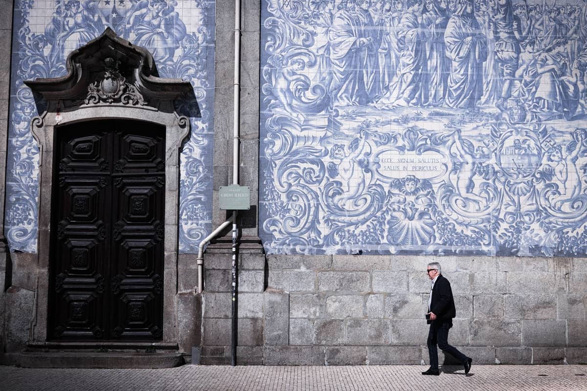 Mann, der an der berühmten blau-weiß gekachelten Azulejo-Fassade eines historischen Gebäudes in Porto, Portugal, vorbeiläuft.
