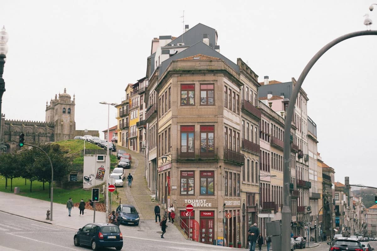 Breite Stadtstraße im historischen Zentrum von Porto mit bunten Fassaden, spazierenden Menschen und der Kathedrale von Porto im Hintergrund.