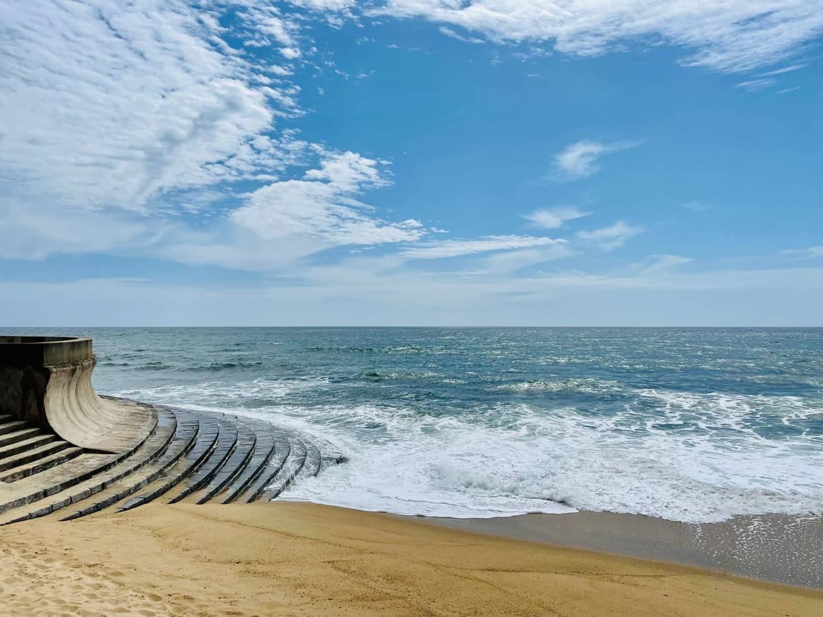 Mur moderniste en béton et marches de piscine courbés vers la plage de sable atlantique sous un ciel bleu sur le littoral de Porto