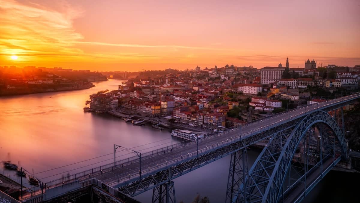 Die Brücke Dom Luís I in Porto bei Sonnenuntergang, die den Fluss Douro überspannt, mit der Skyline der Stadt und historischen Gebäuden im Hintergrund.