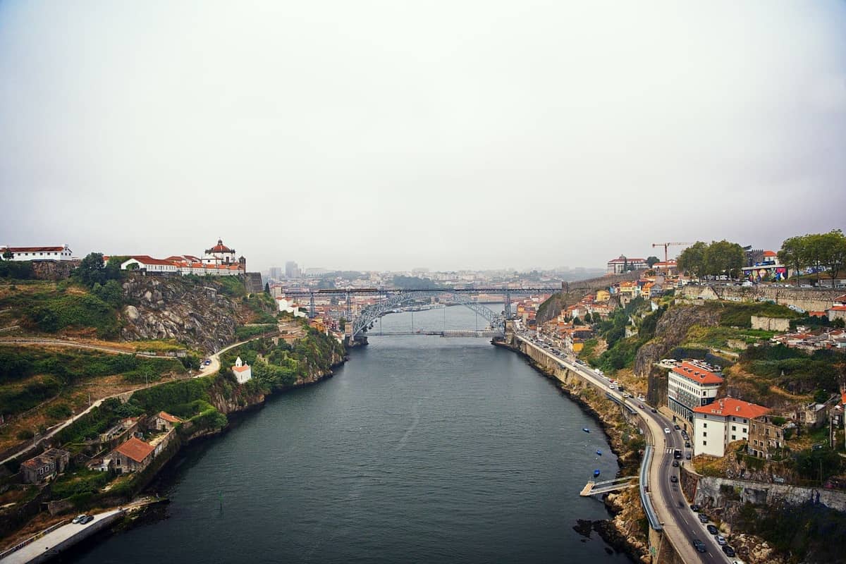 Erhöhter Panoramablick auf den Douro in Porto mit mehreren ikonischen Brücken, beiden Flussufern und Portos Stadtlandschaft am Hang unter einem diesigen Himmel.